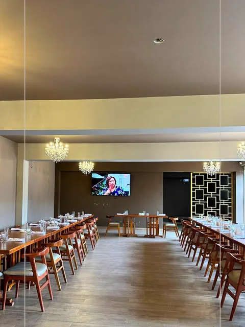Salón amplio de ABRASAR con mesas largas de madera, arañas de cristal y pantalla