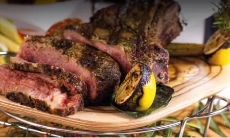 Tomahawk a la parrilla cortado en tajadas sobre una tabla con limón asado